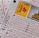 A close-up image of lottery tickets featuring crossed-out numbers, brand logos, and various numbers in a grid format. The tickets have sections for different games, and numbers are marked with black crosses.