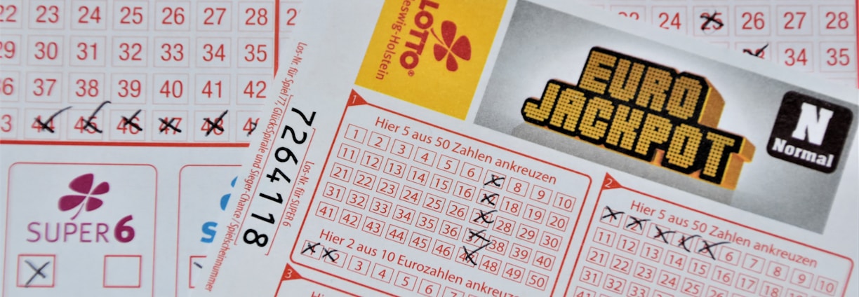 Three lottery tickets are displayed, including Eurojackpot and Super 6. Various numbers are marked on the tickets, with some crossed out and others checked. The Eurojackpot ticket is partially visible with the logo prominently displayed, and a ticket number is visible on one of the tickets.
