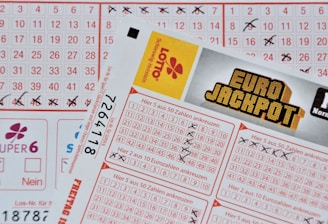 Three lottery tickets are displayed, including Eurojackpot and Super 6. Various numbers are marked on the tickets, with some crossed out and others checked. The Eurojackpot ticket is partially visible with the logo prominently displayed, and a ticket number is visible on one of the tickets.
