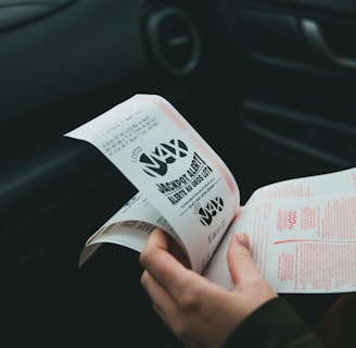 A person is holding and examining what appears to be lottery tickets inside a car. The image is focused on the tickets and the person's hands, with parts of the car interior visible in the background.